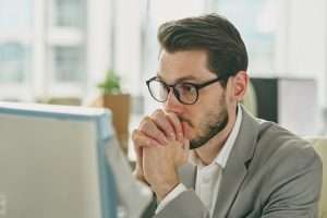 Young pensive businessman cannot understand information on computer screen